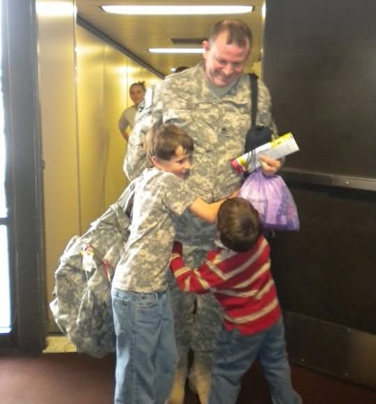 A man arriving at an airport, greeted to two small boys.